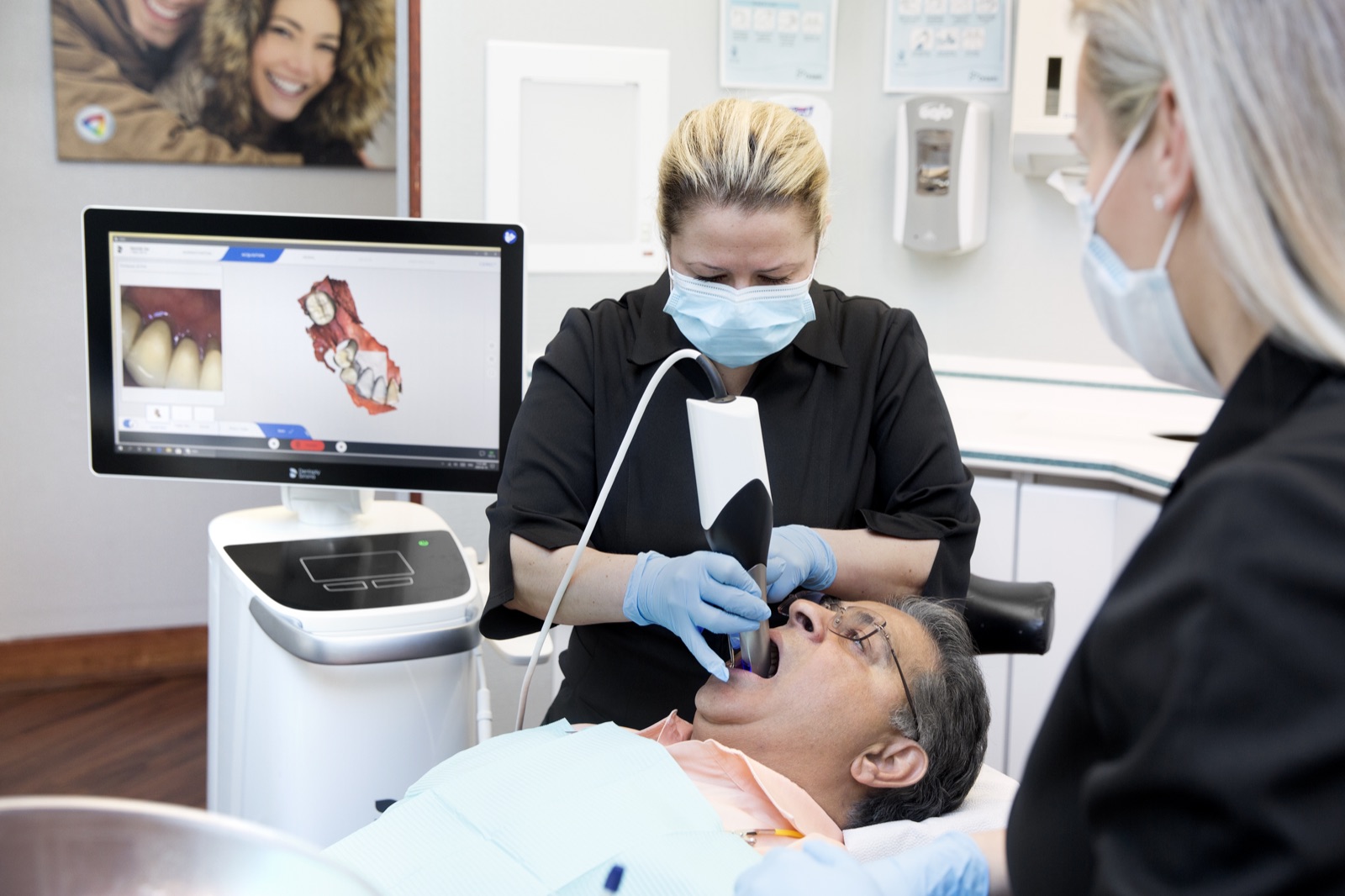 A digital intraoral scan being taken, with the 3D model building on screen beside the chair