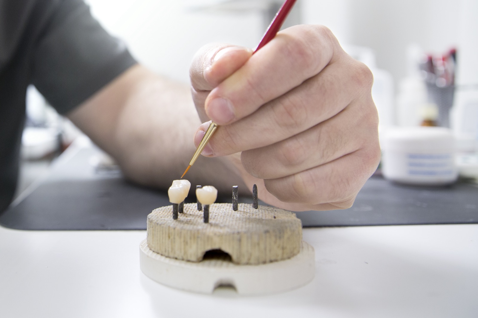 A technician hand-shading porcelain crowns on a firing tray in our laboratory