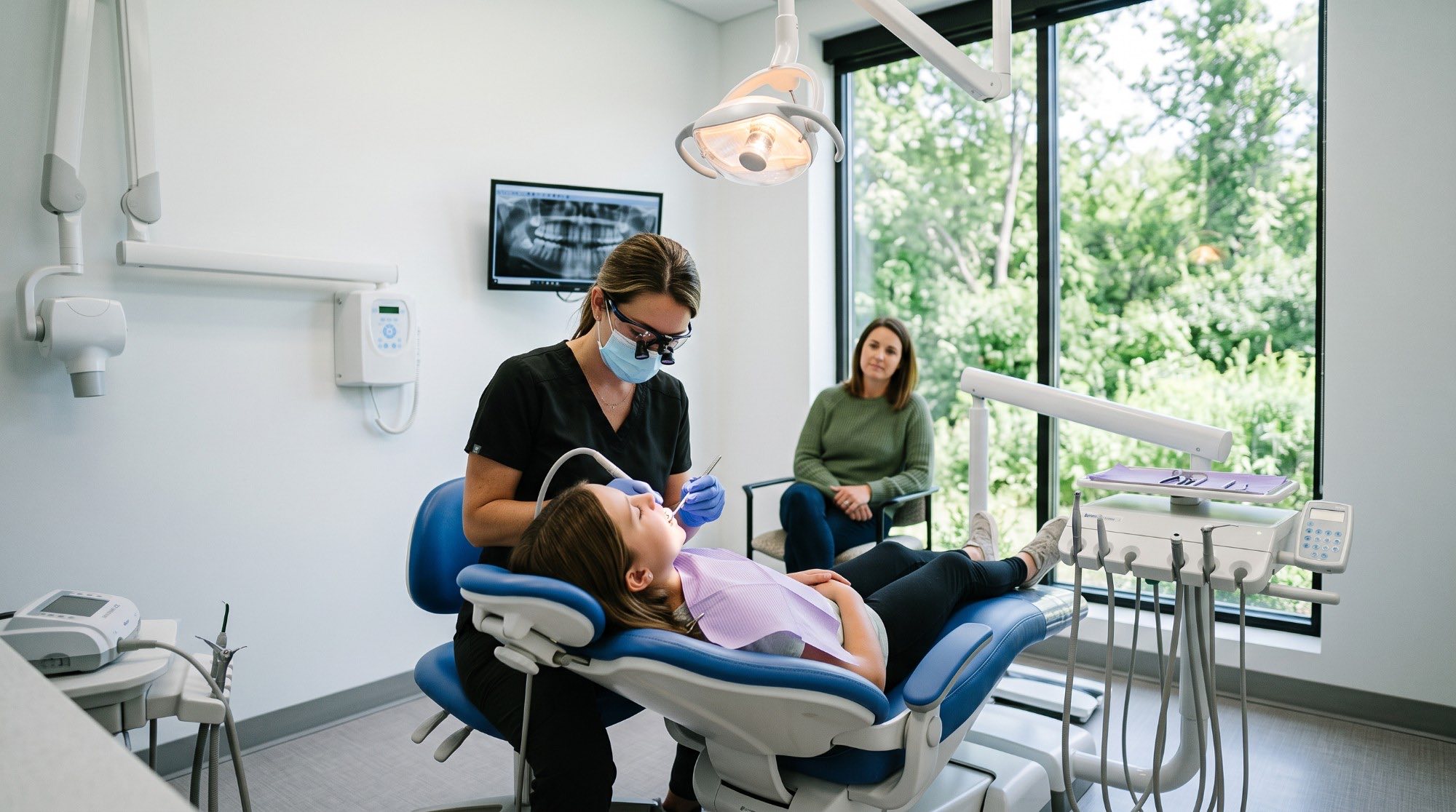 A child having their teeth checked, with a parent sitting beside the chair